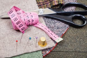 dressmaking still life - pink measure tape, pins, thimble, shears on fabrics